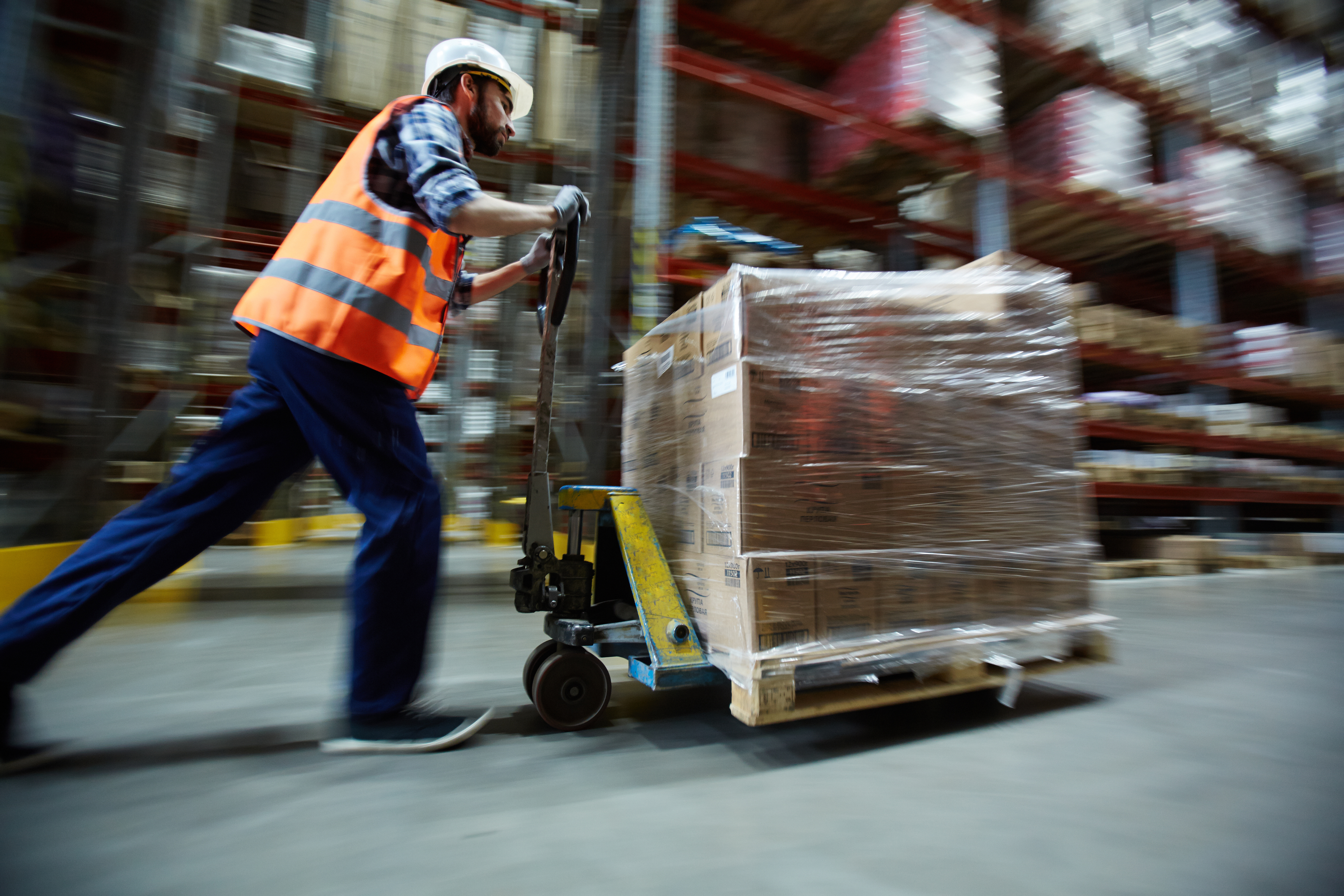 Warehouse worker pushing manual pallet jack through a warehouse